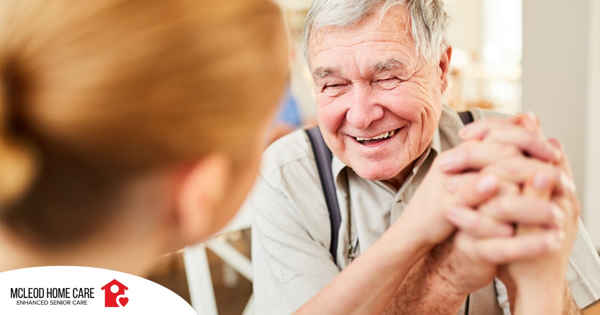 A caregiver holds hands with a happy older client, representing the results of creating a comfortable environment in the home.