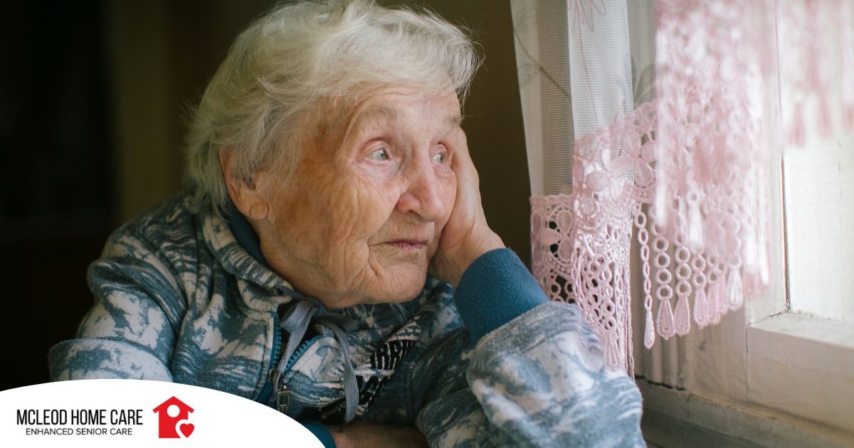 An older woman peacefully looks out of the window while the sun is still up, representing what can happen with sundowning.